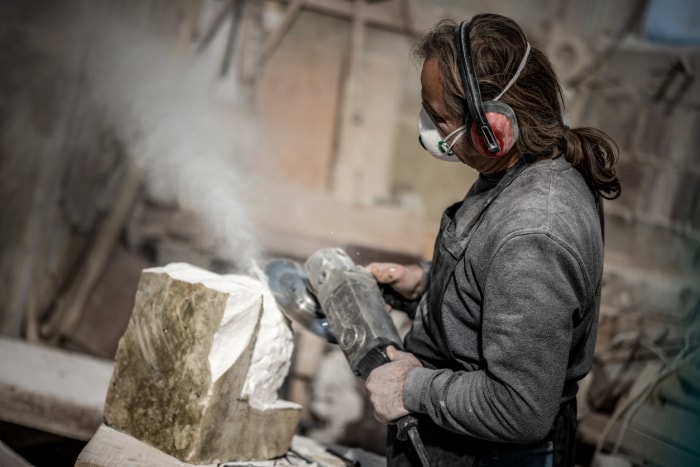 Une personne utilise une scie à main pour couper un bloc de pierre tout en portant un masque.