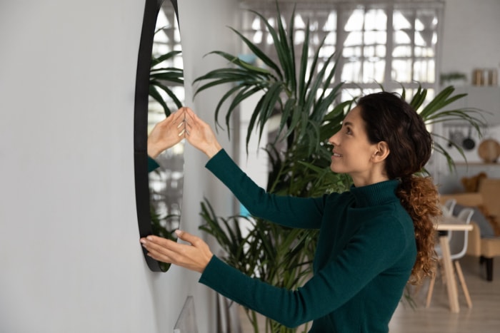 Une femme latine souriante du millénaire pose un miroir sur le mur pour décorer un salon confortable et emménager dans une nouvelle maison ou un nouvel appartement. Une jeune femme hispanique heureuse rénove sa propre maison. Rénovation, concept de design.