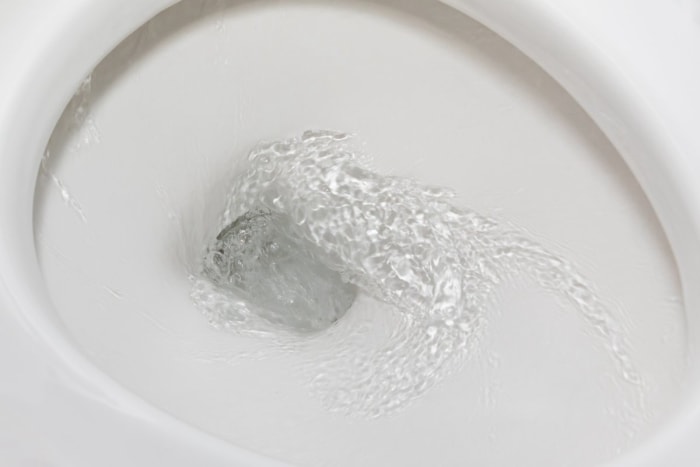 Une cuvette de WC blanche est à mi-chute, l'eau s'écoulant en spirale le long de la porcelaine propre.