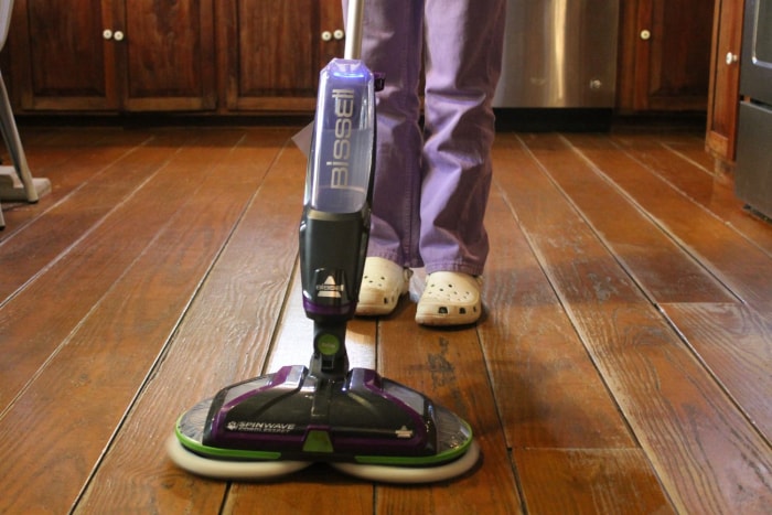 Une personne utilisant la brosse à récurer Bissell SpinWave pour nettoyer un plancher en bois.