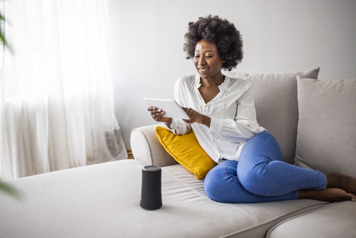 iStock-1321422469 remboursements d'impôts amélioration de l'habitat Une jeune femme heureuse contrôle des appareils domestiques intelligents avec des commandes vocales et un haut-parleur intelligent à la maison