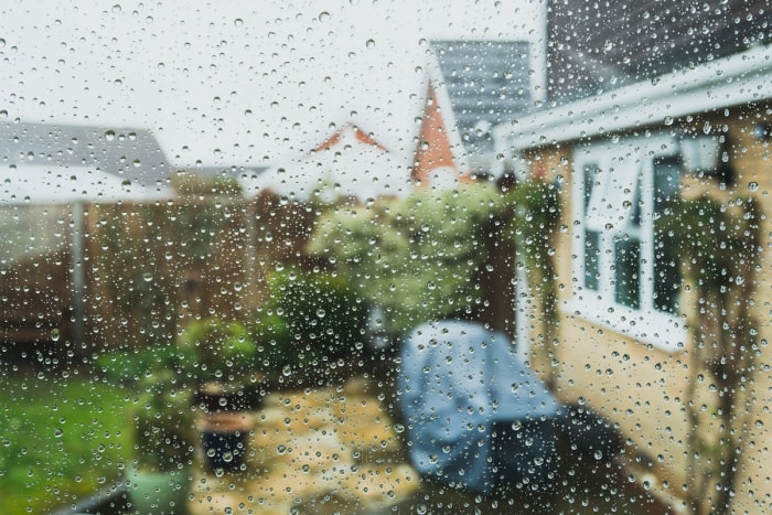 Une fenêtre avec des gouttes de pluie donnant sur un patio pendant un orage.