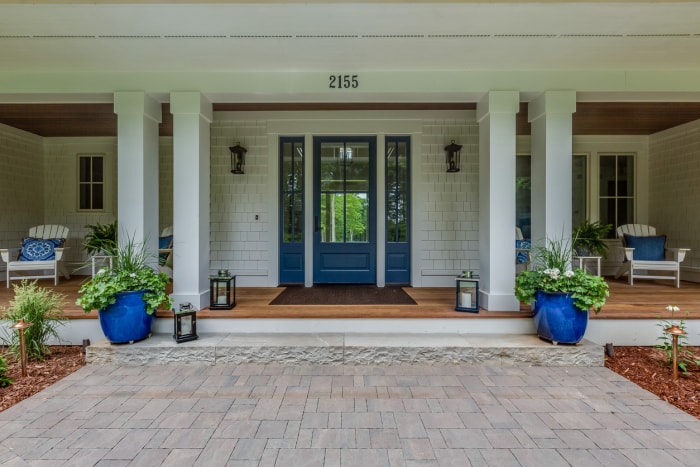 grand porche élégant sur une maison blanche avec porte bleue et pot de fleurs bleu et accents d'oreiller