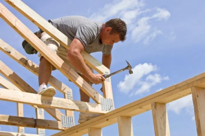 Un homme cloue la charpente d'une maison