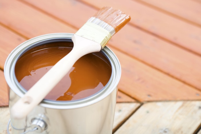 Un pinceau est posé sur une boîte de conserve remplie de teinture pour bois.