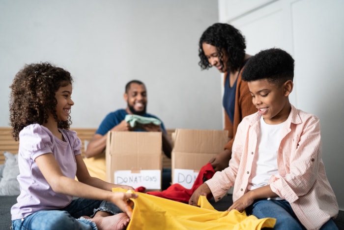 Des parents avec leurs enfants trient des vêtements dans des boîtes pour les donner à la maison.