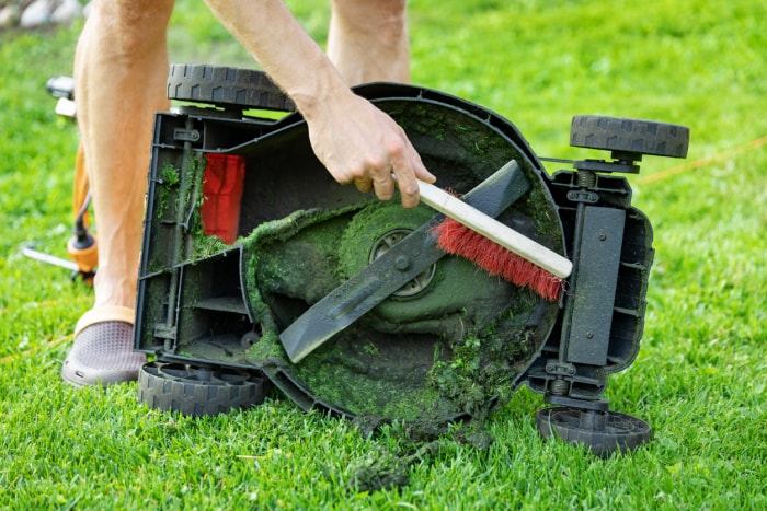 Un homme nettoie le dessous d'une tondeuse à gazon avec une brosse à poils.