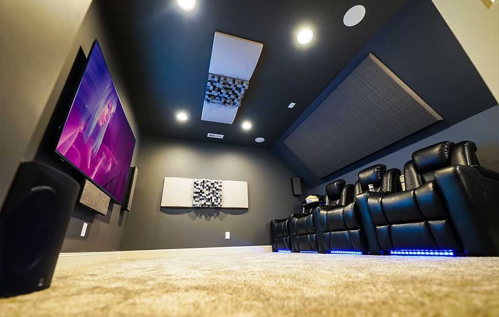 Petit home cinéma avec quatre fauteuils en cuir noir, panneau acoustique, grande télévision