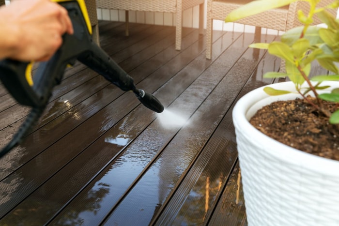 Gros plan d'une personne nettoyant une terrasse au jet d'eau. 