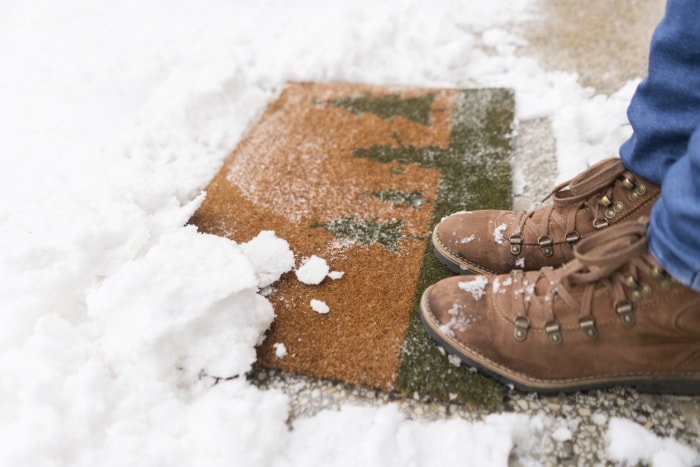 Les bottes d'hiver d'un homme debout dehors sur un paillasson dans la neige.