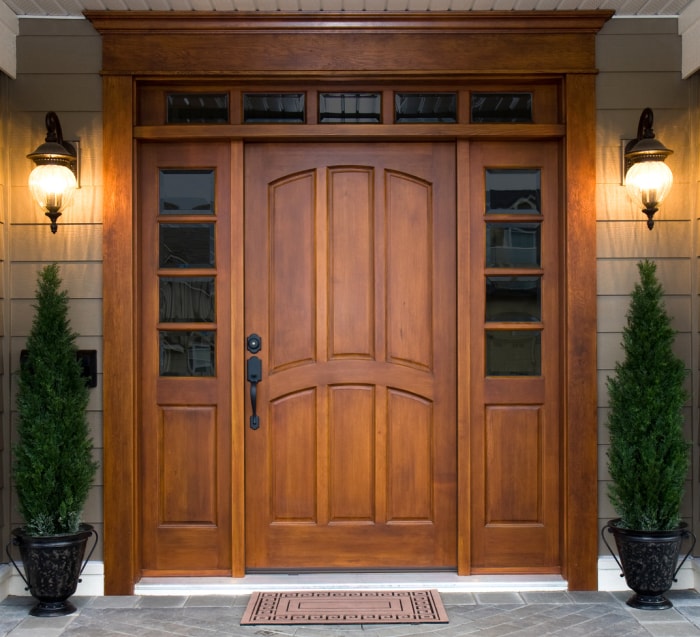 belle porte d'entrée en bois foncé flanquée de deux lumières de maison sur le porche avant