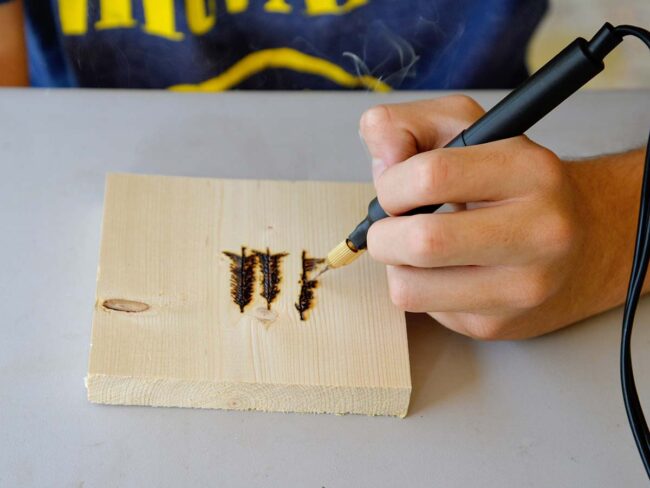 Un adolescent dessine des arbres à l'aide d'un outil de combustion du bois