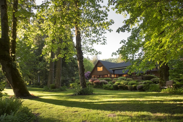 La façade d'une maison brune avec plusieurs arbres, arbustes et plantes comme aménagement paysager.