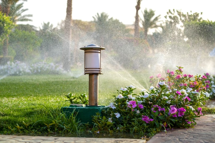 erreurs d'aménagement paysager qui font que les acheteurs de maisons font demi-tour fleurs bordant le chemin de pierre sur la pelouse système d'arrosage sur la pulvérisation d'eau