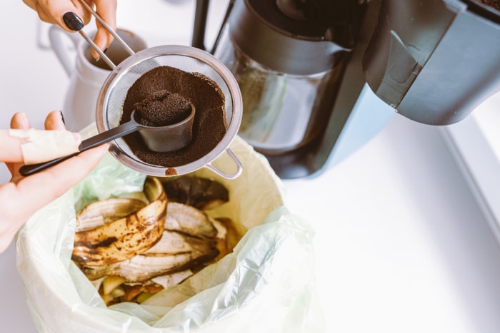 Du vieux marc de café est jeté dans un bac à compost à côté d'une cafetière.