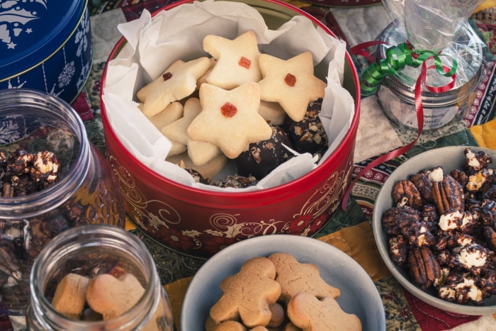 Vue aérienne colorée de divers biscuits sablés et de pain d'épices dans des boîtes et de pop-corn au chocolat et de bordeaux aux canneberges emballés dans du cellophane, le tout sur un chemin de table matelassé en patchwork.