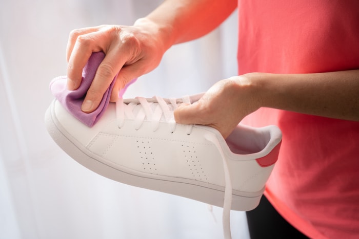 femme nettoyant une chaussure blanche avec un chiffon en microfibre violet