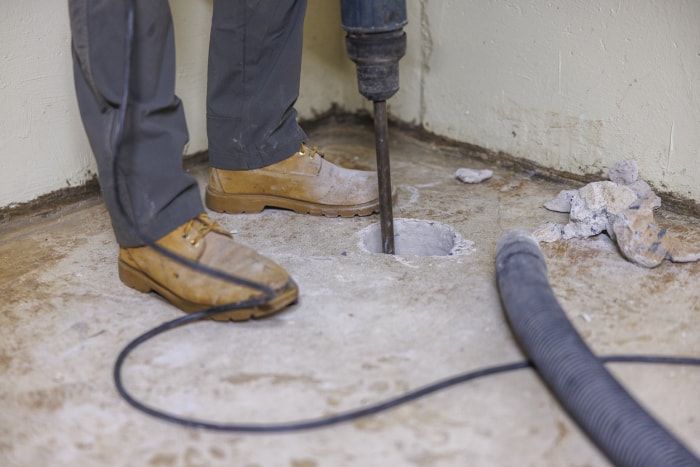 Installation d'un système d'atténuation du radon. Un ouvrier perce un trou dans le plancher du sous-sol pour améliorer la maison.