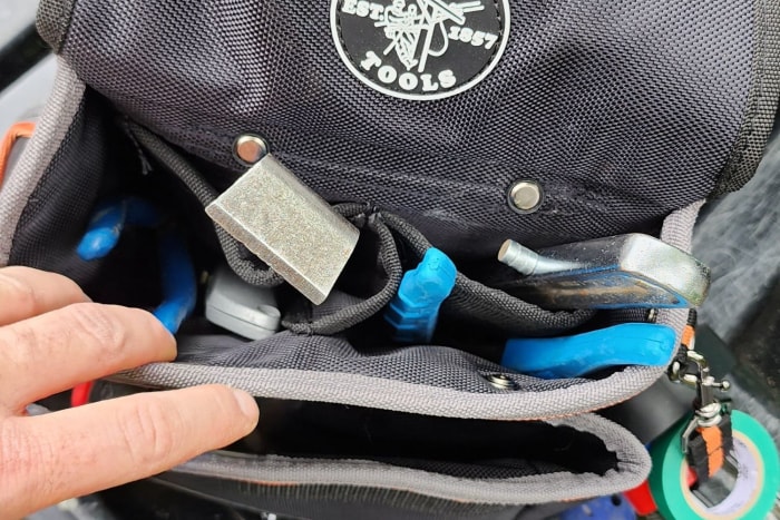 Une personne saisissant un outil de la ceinture d'outils d'électricien Tradesman Pro de Klein Tools.