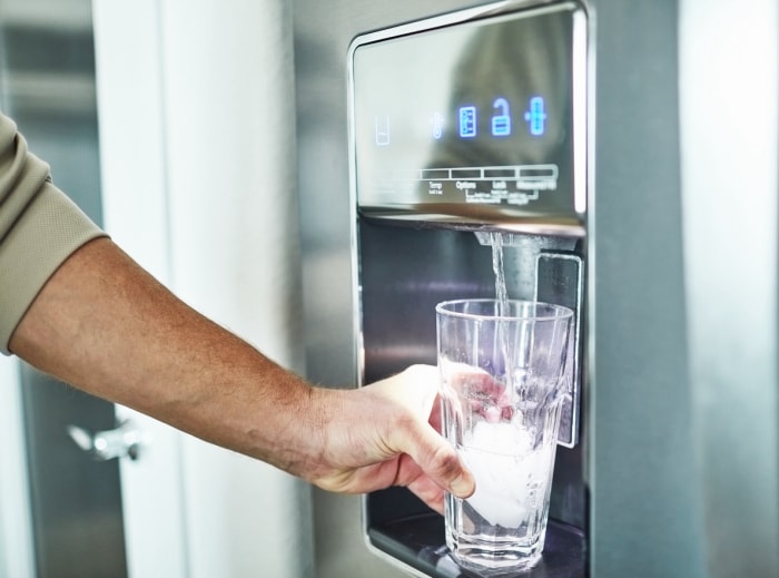 iStock-1300229763 L'agent immobilier ne veut pas que l'homme remplisse le verre du distributeur d'eau du réfrigérateur