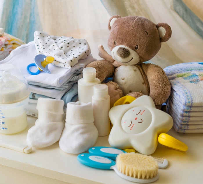 produits pour bébé posés sur une commode blanche, dont un ours en peluche marron, une tétine, un jouet en forme d'étoile, des chaussures pour bébé et un biberon