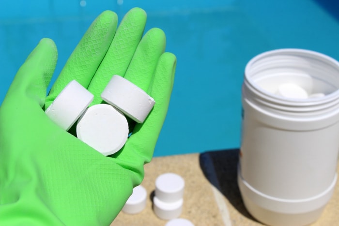 Tenant des comprimés de choc de piscine blanc tout en portant des gants verts.