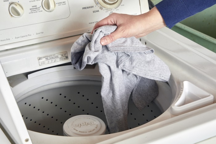 Une femme laisse tomber des vêtements dans une machine à laver.