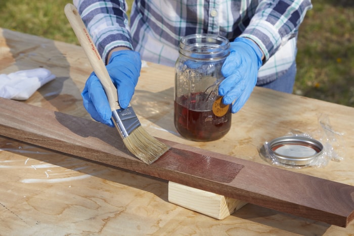 Une femme utilise un pinceau à poils naturels pour appliquer un produit d'étanchéité à l'huile sur une planche de bois.