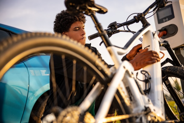 une jeune personne travaille sur le compartiment batterie d'un vélo électrique en plein air