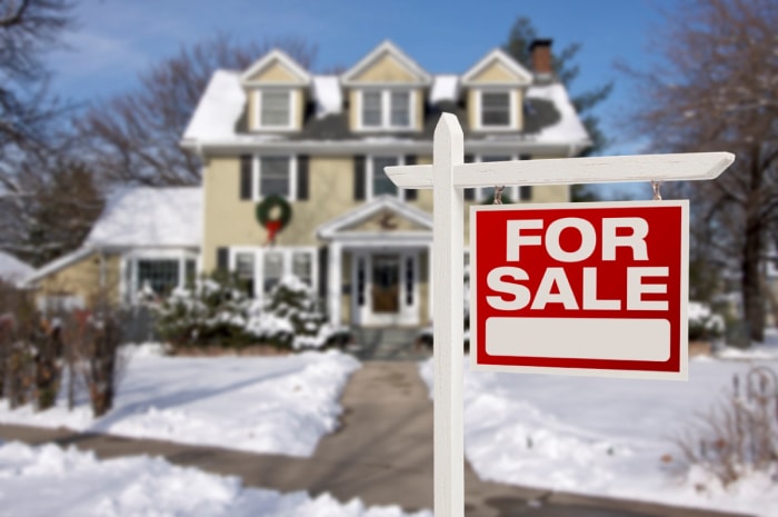 Un panneau « à vendre » est placé devant une maison recouverte de neige.