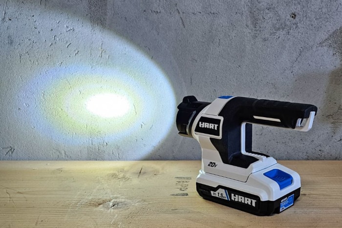 La lampe LED sans fil Hart Tools sur une table de travail et éclairant un mur en ciment.