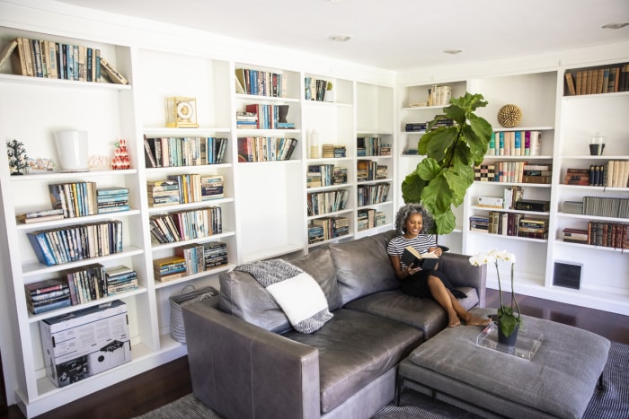 Une femme noire lisant un livre dans sa bibliothèque à la maison