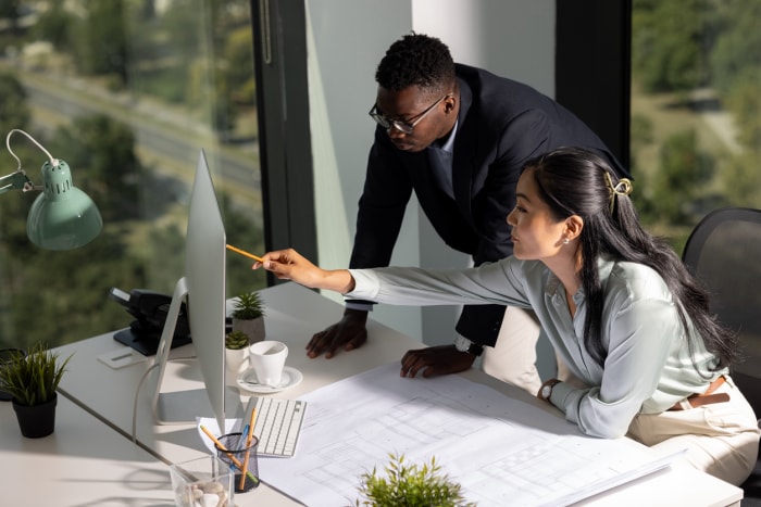 deux architectes au bureau travaillant à un bureau avec un ordinateur et des plans