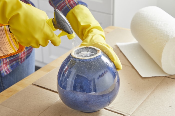 Une femme vaporise un spray dissolvant d'adhésif sur un autocollant au fond d'un pot.