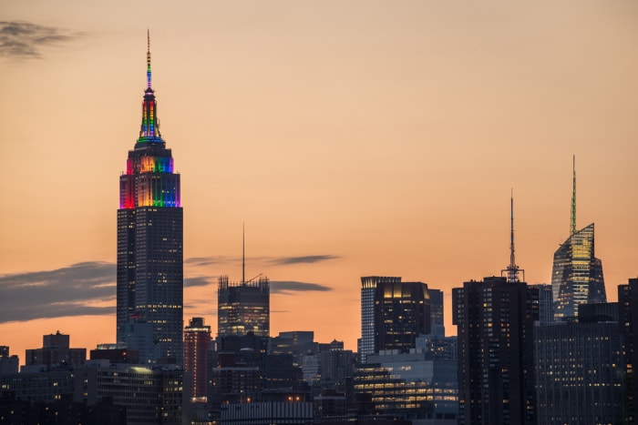 Une partie de l'horizon de Midtown Manhattan avec l'Empire State Building affichant les couleurs de la fierté prise depuis Brooklyn juste avant le coucher du soleil.