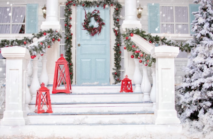 Cour enneigée avec porche de Noël, véranda, couronne, sapin de Noël, guirlande, boules de Noël et lanternes.