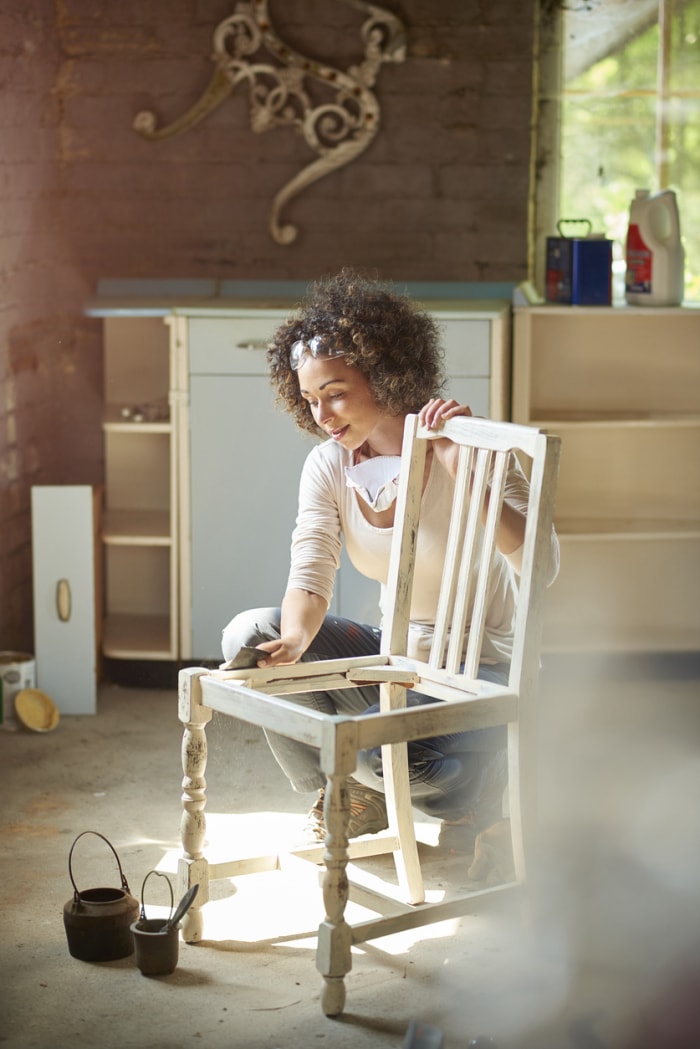 femme dans un atelier essuyant un cadre de chaise en bois blanc antique avec un chiffon collant