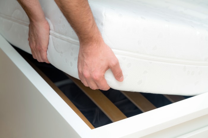 L'homme soulève le matelas dans la chambre à coucher. Il regarde le cadre du lit et inspecte le matelas