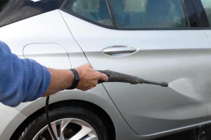 gros plan d'un homme utilisant un nettoyeur haute pression pour laver une voiture grise