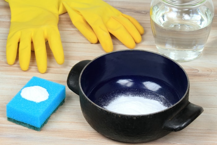 Pot en émail bleu foncé nettoyé avec du bicarbonate de soude, une éponge et des gants en caoutchouc.