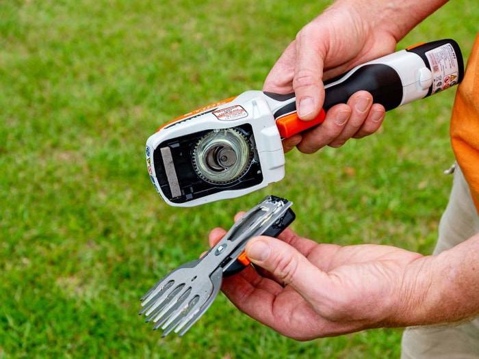 Un homme montre les têtes de coupe à changement rapide stockées dans la plaque de base de la cisaille de jardin sans fil Stihl.