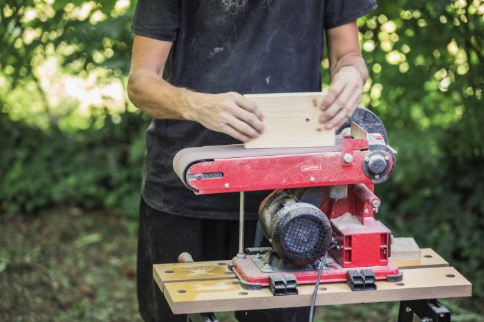 iStock-1336057225 comment utiliser une ponceuse à bande Artisan ponçant un bloc de bois à l'aide d'une ponceuse à bande à disque combinée