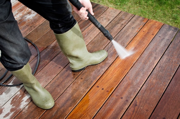 Gros plan d'une personne portant des bottes vertes nettoyant une terrasse au jet d'eau.