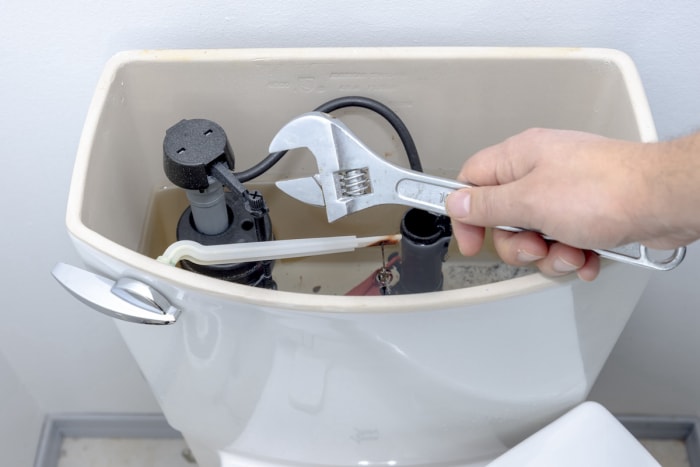 Une personne tenant une clé à proximité d'un réservoir de toilettes ouvert pour effectuer une réparation de plomberie par elle-même.