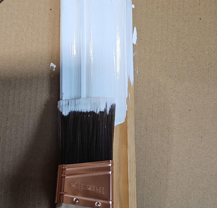 Le pinceau à peinture Purdy XL Glide de 2 pouces utilisé pour peindre une garniture en bois en blanc.