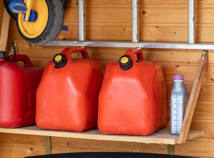 Bidons d'essence rouges stockés sur une étagère en bois.