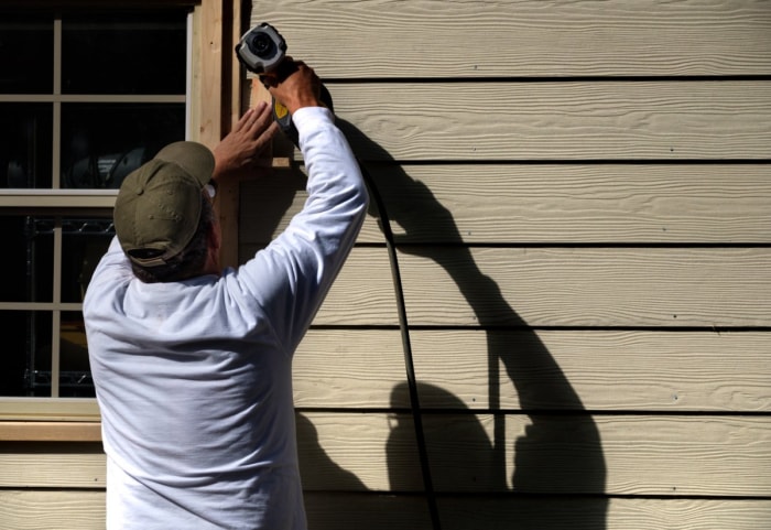 Un ouvrier utilise un pistolet à clous pour installer le bardage d'une maison.