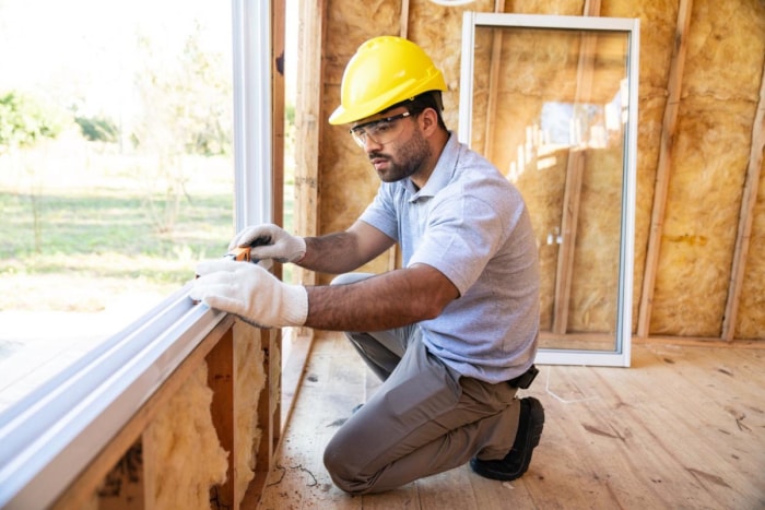 Un ouvrier portant un casque jaune installe une fenêtre dans une maison en construction.