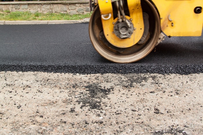 Un rouleau lisse une allée en asphalte nouvellement pavée.