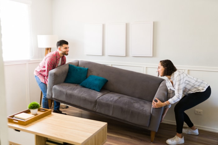 Jeune couple joyeux effectuant des travaux d'aménagement et déplaçant leur canapé dans le salon tout en le décorant